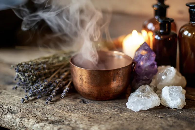 Copper cauldron releasing steam beside lavender bundle and crystals on wooden table