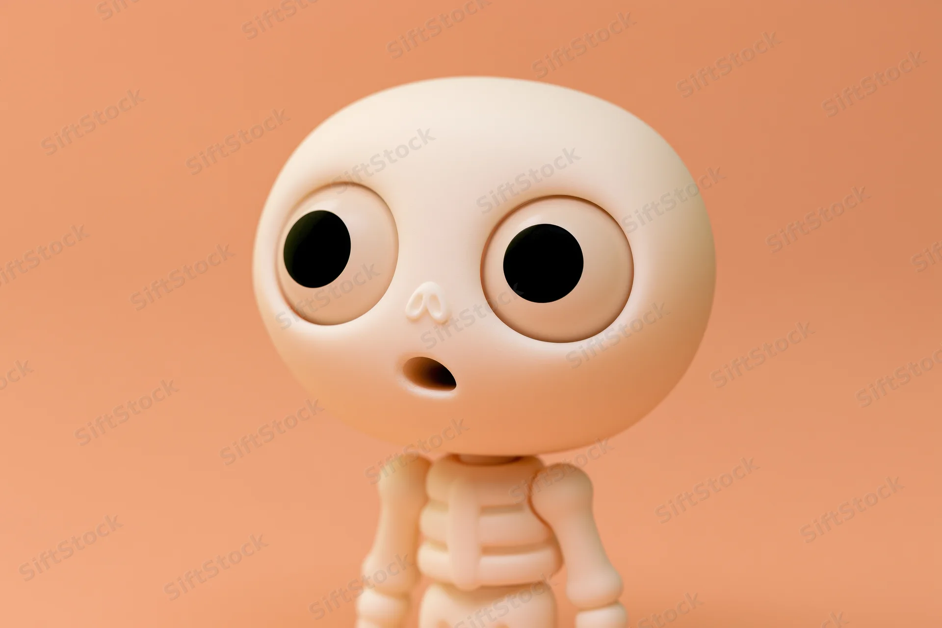 Cute cartoon skeleton toy figurine with oversized eyes standing against peach background