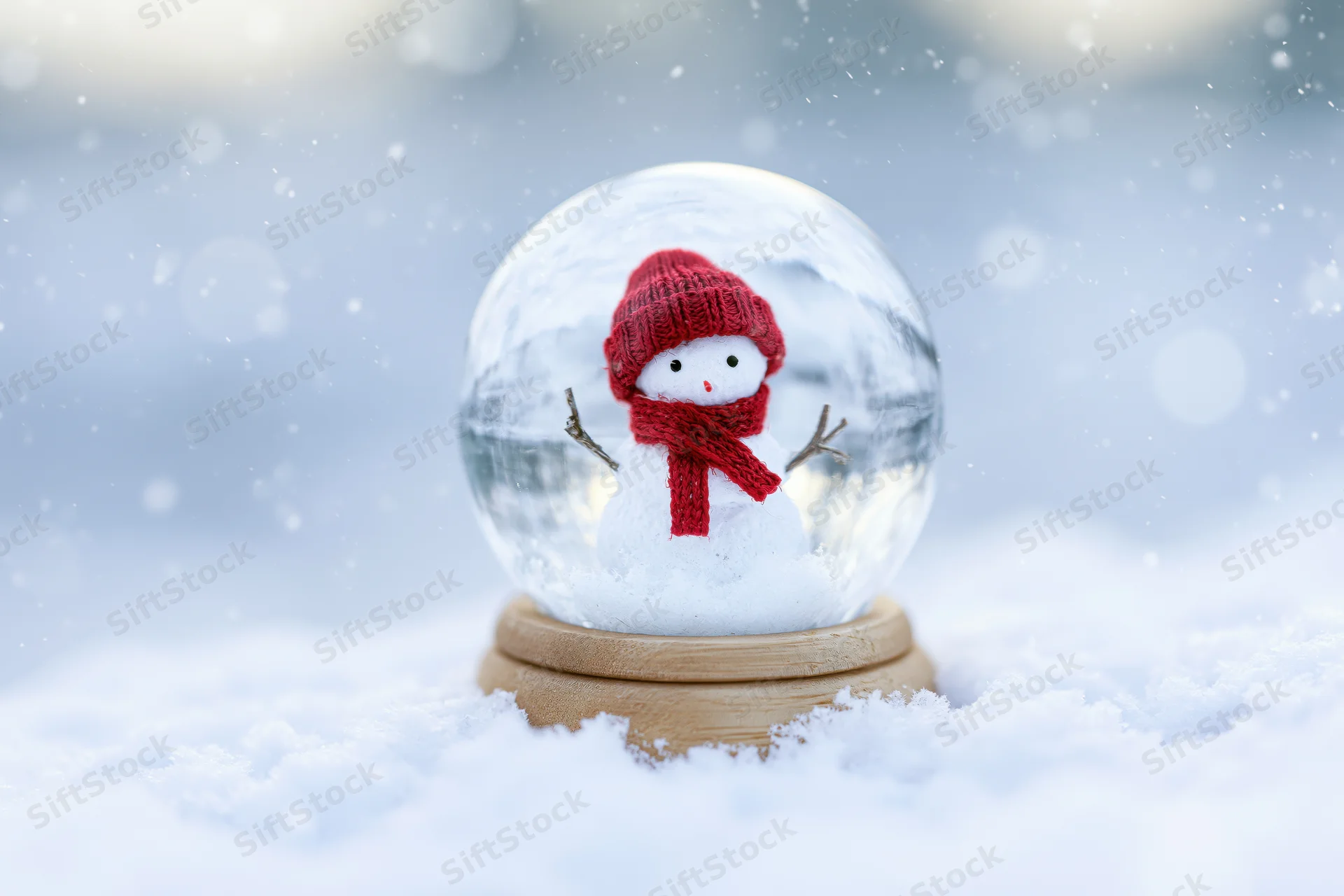 Snowman figure in red hat and scarf inside glass snowglobe resting on snow-covered ground outdoors