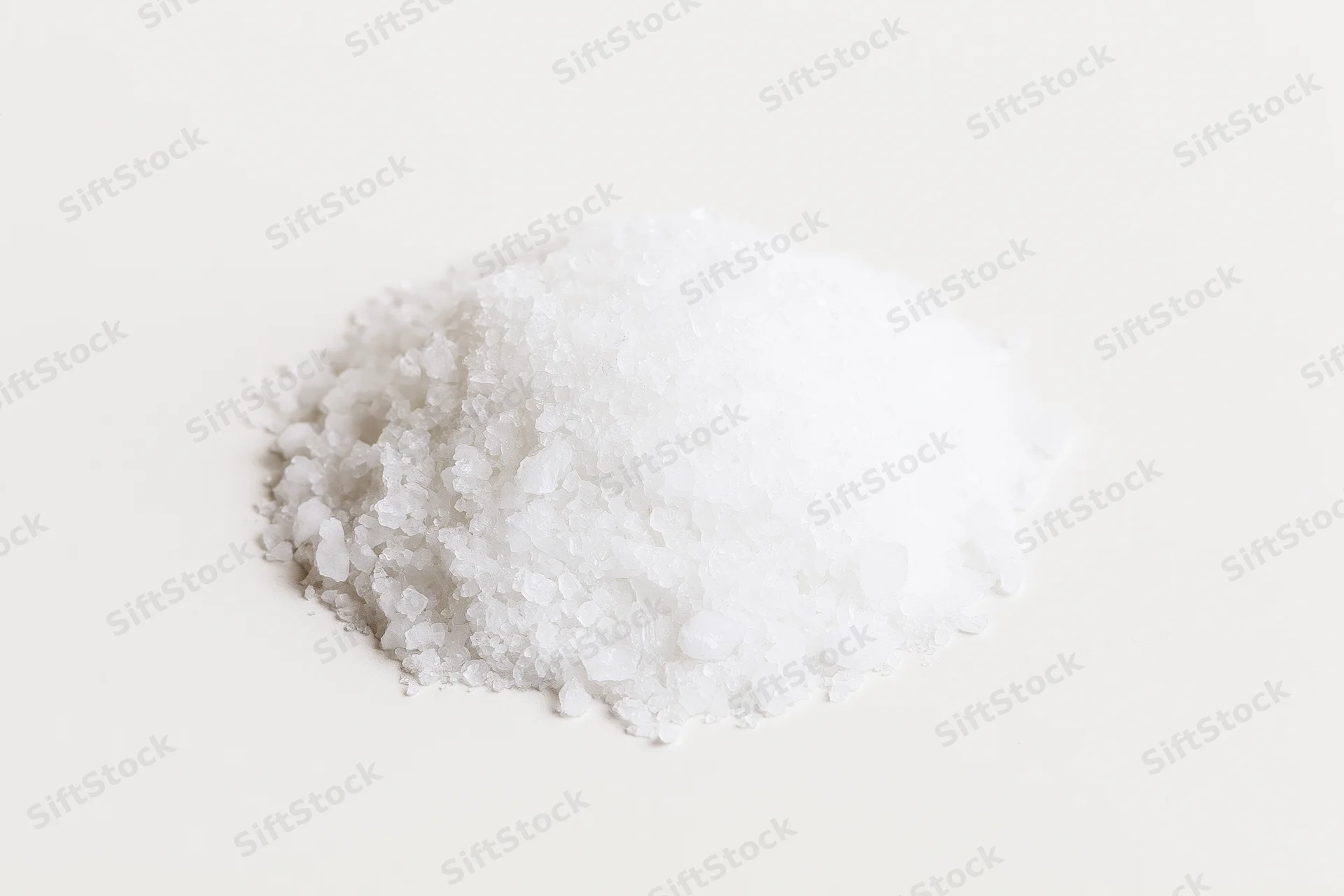 A heap of coarse white salt crystals on a plain white surface