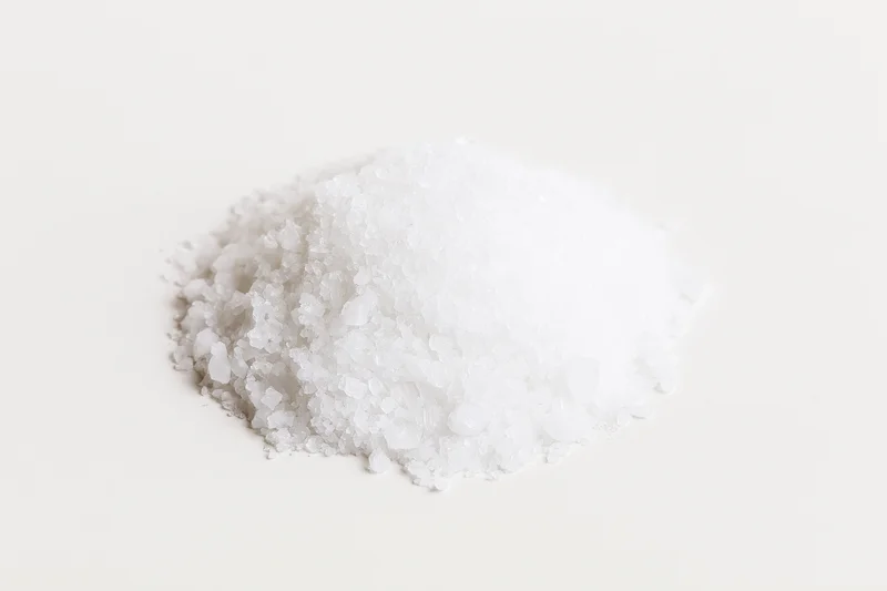 A heap of coarse white salt crystals on a plain white surface