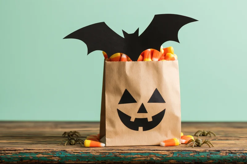 Paper bag decorated with jack-o-lantern face and bat wings filled with candy corn on wooden table