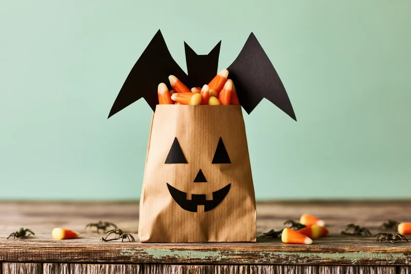 Kraft paper bag decorated with jack-o-lantern face and bat wings filled with candy corn on wooden table