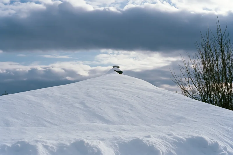 Snow-covered hill with chimney at summit under cloudy sky