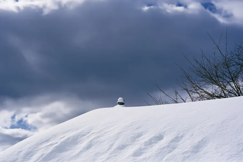 Snow-covered chimney pot on a snowdrifted roof under cloudy sky