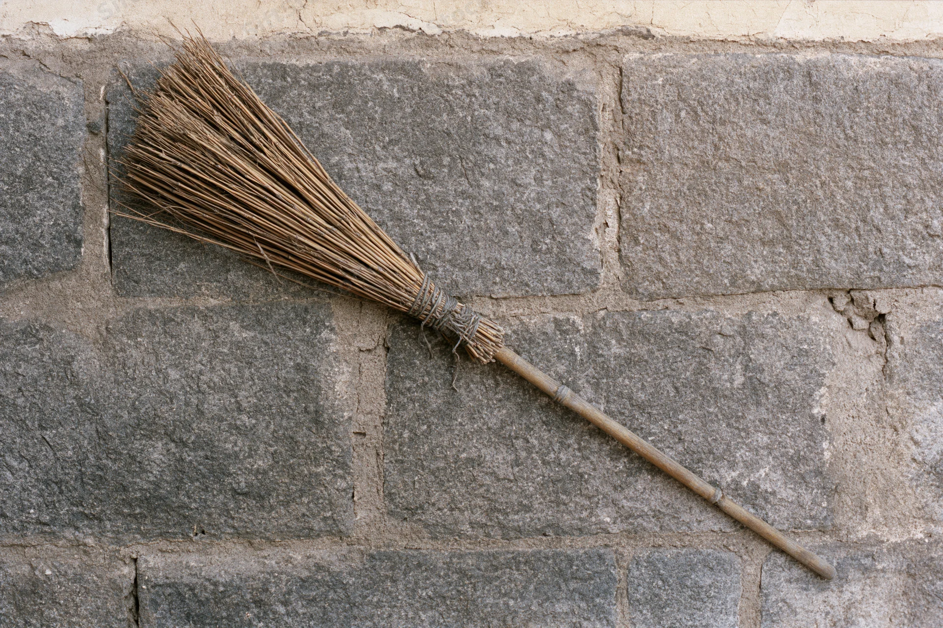 Traditional bamboo broom leaning against rough stone wall
