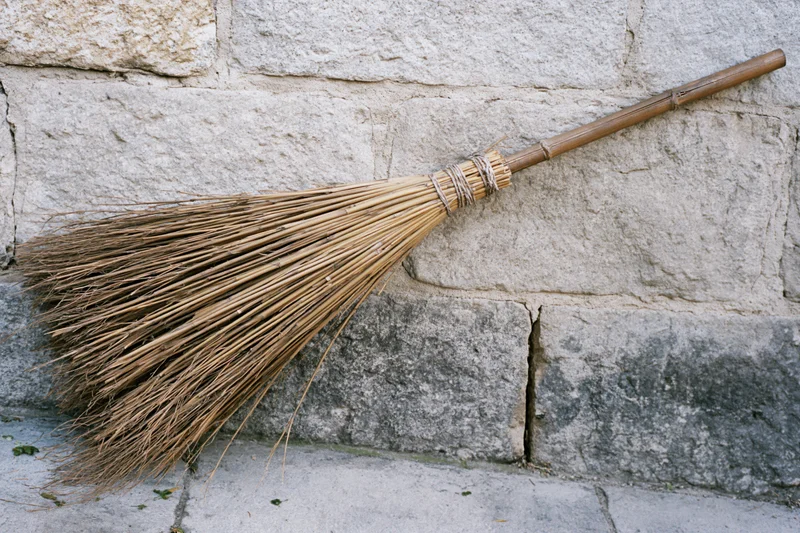 Traditional bamboo broom leaning against rough stone wall outdoors