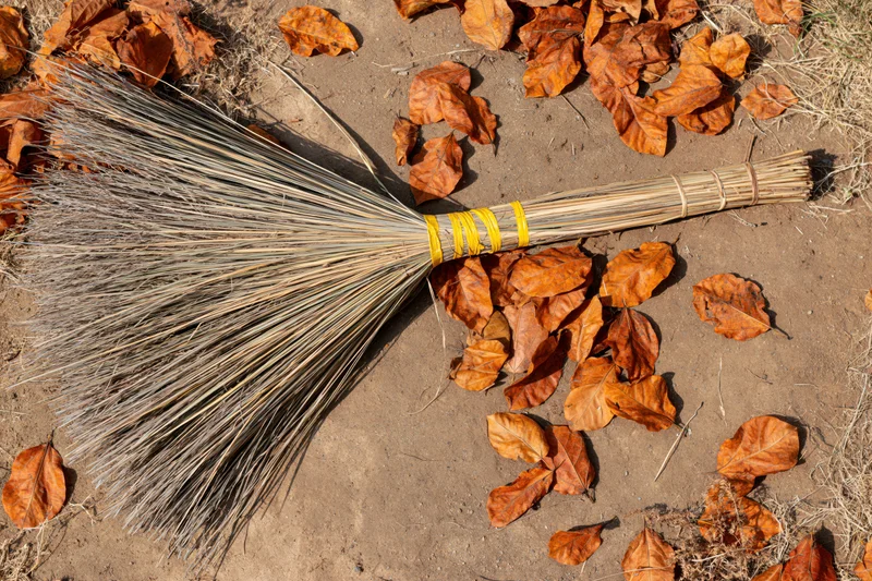 Traditional hand-tied straw broom lying on dry earth among fallen autumn leaves