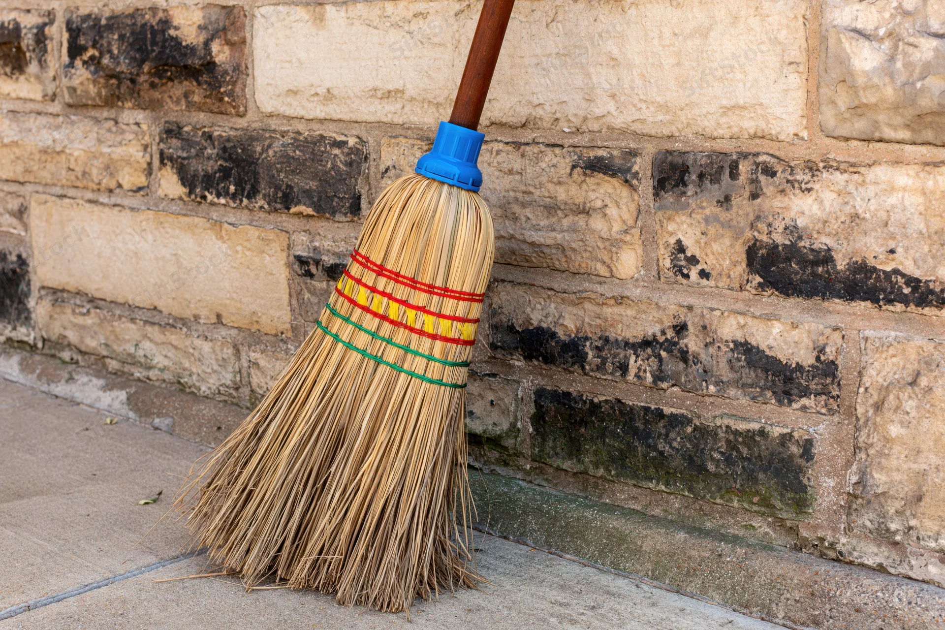 Traditional straw broom with colorful bindings leaning against a weathered stone wall outdoors