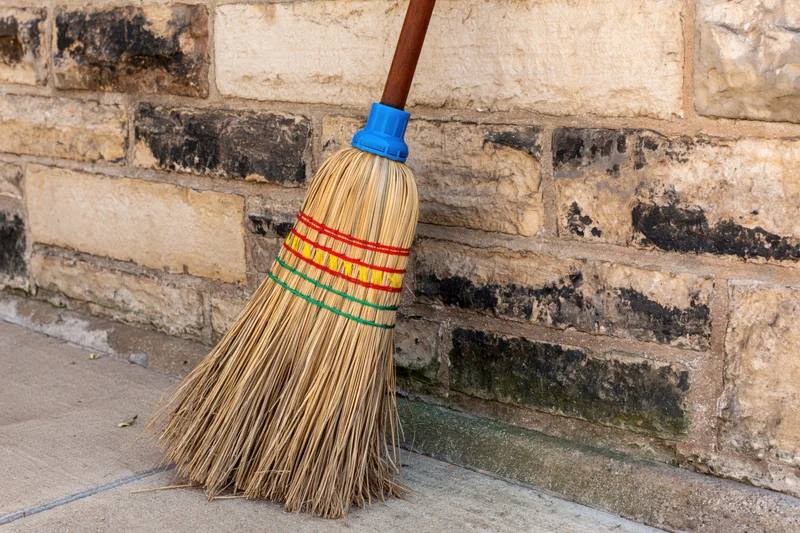 Traditional straw broom with colorful bindings leaning against a weathered stone wall outdoors