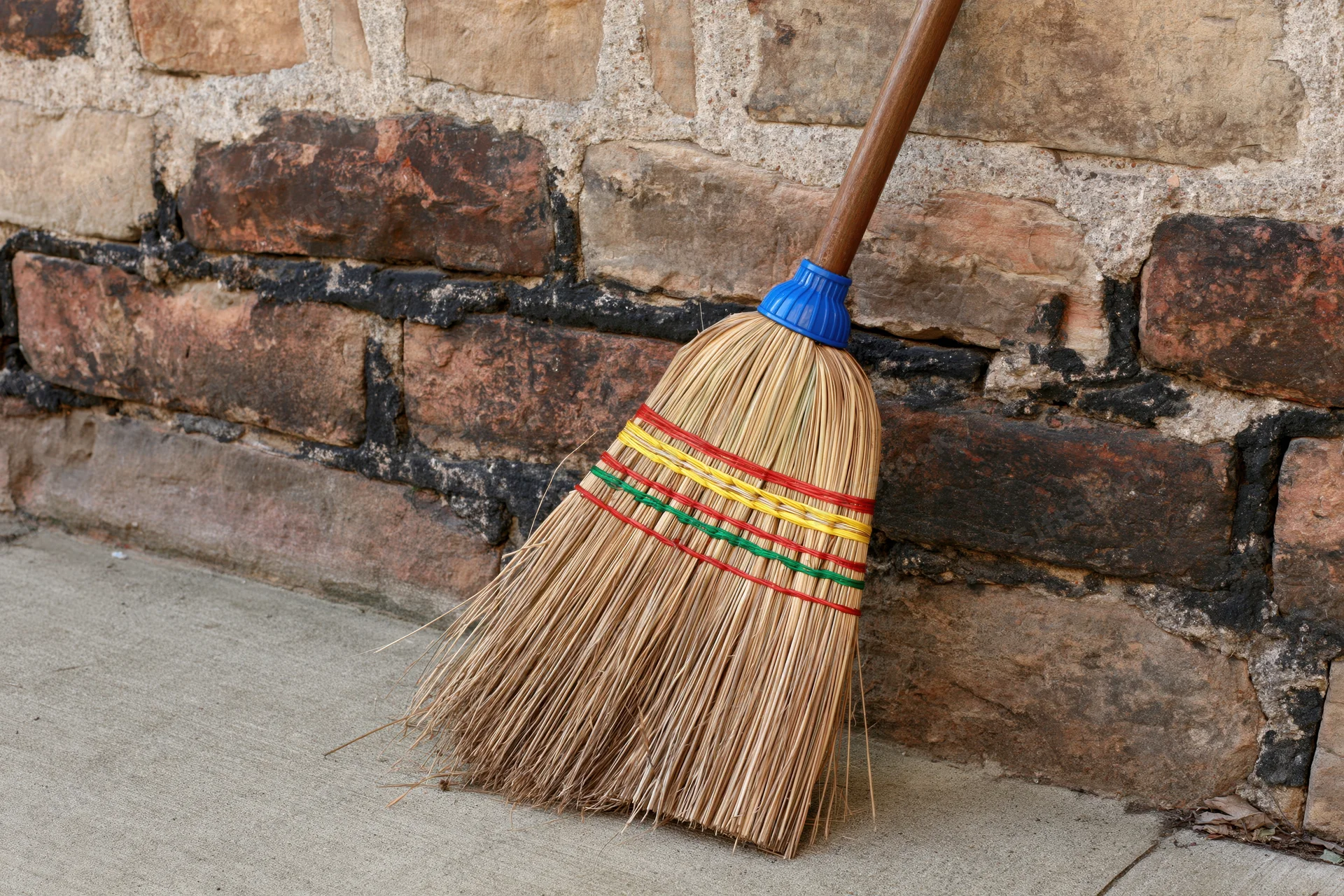 Traditional straw broom with colorful bands leaning against a brick wall outdoors