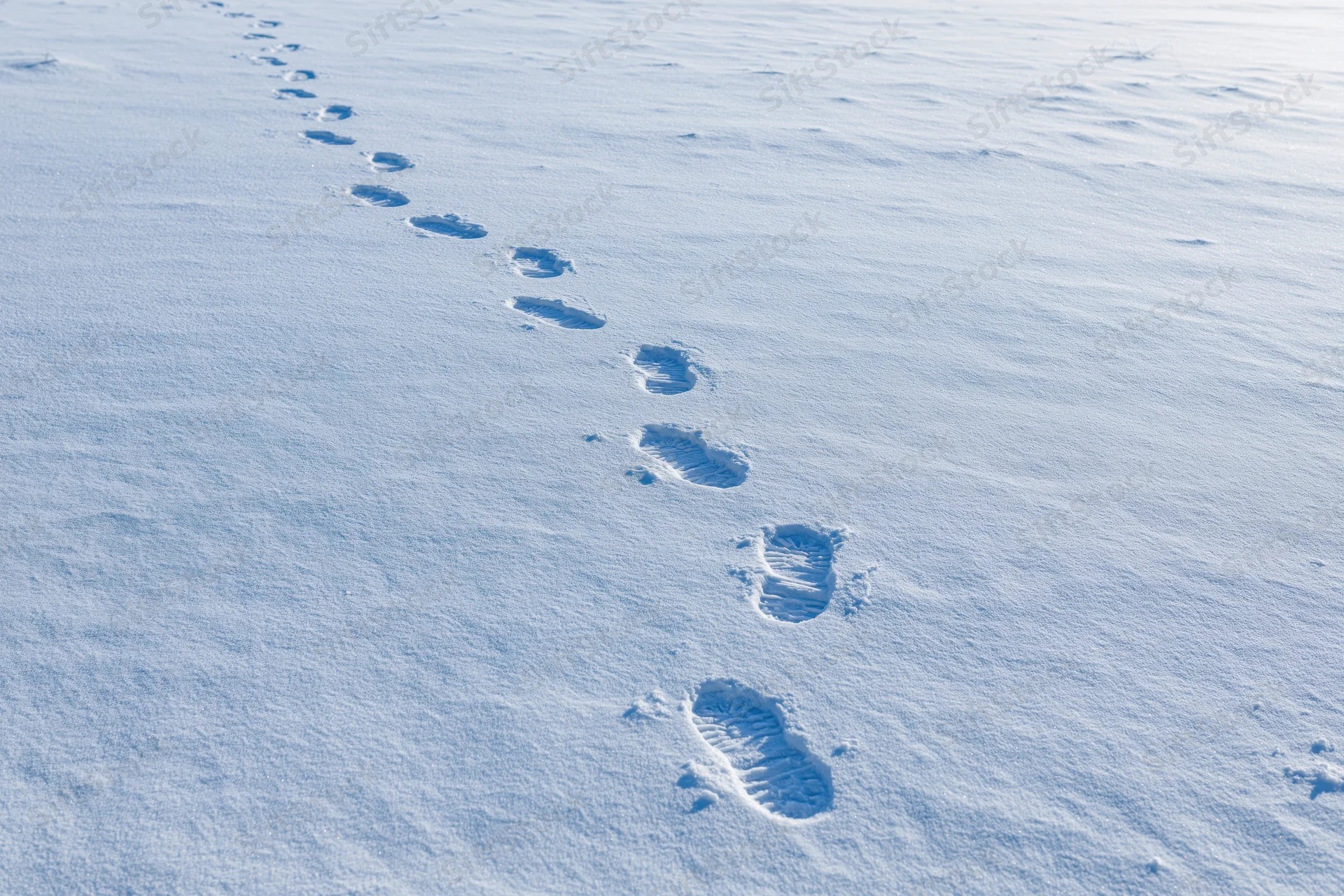 A trail of human footprints in fresh undisturbed snow across a snowy landscape