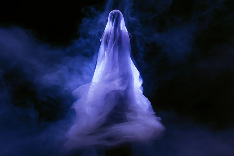Translucent ghostly figure draped in billowing sheer fabric floating in dark blue smoke