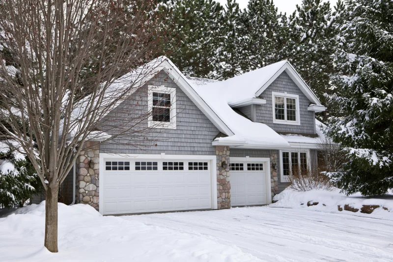 Gray cedar shake suburban house with two-car garage and snow-covered driveway in winter