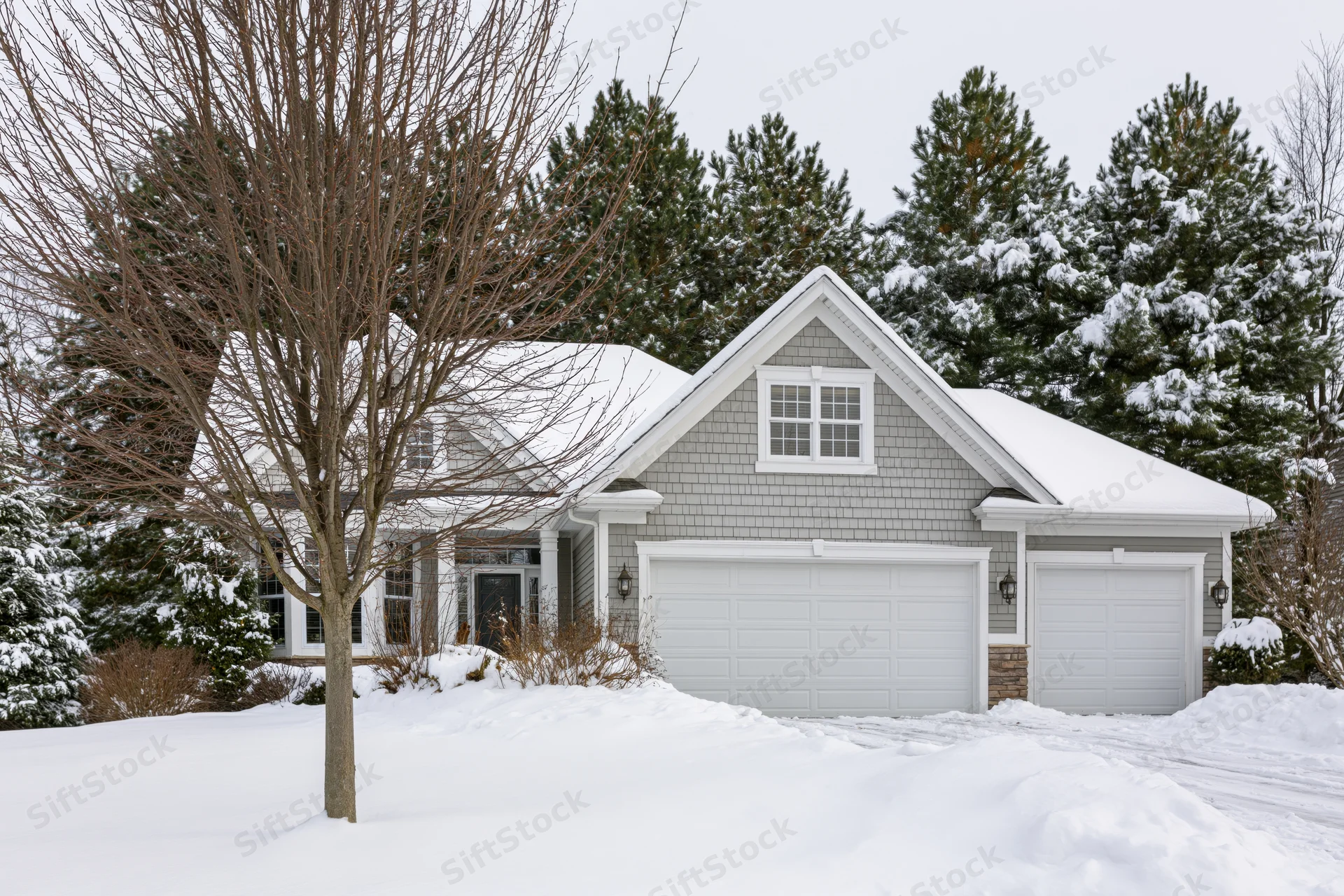 Gray cedar shake suburban house with two-car garage covered in snow, front exterior view