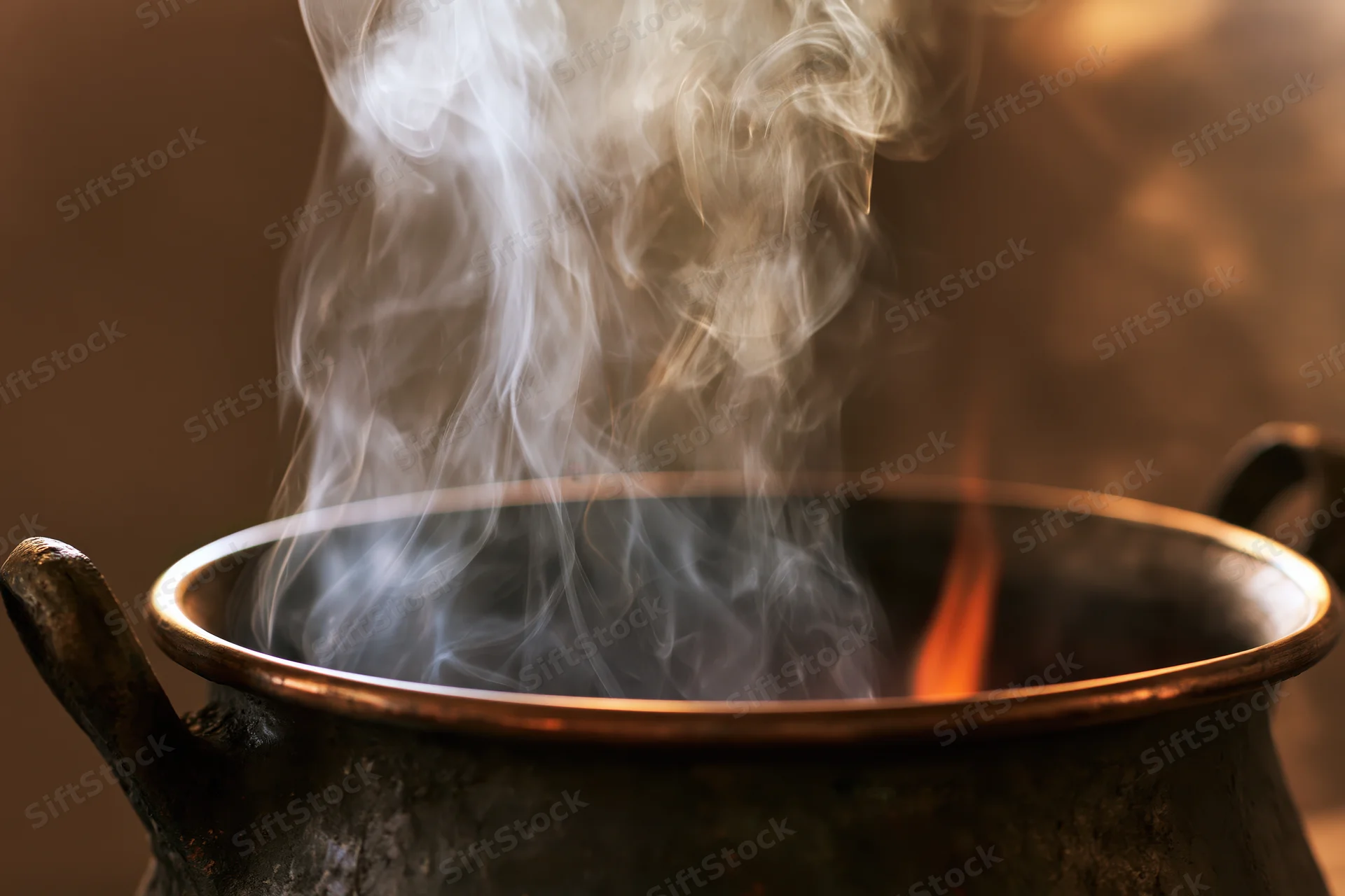 Weathered brass cauldron with steam rising over fire in dark setting
