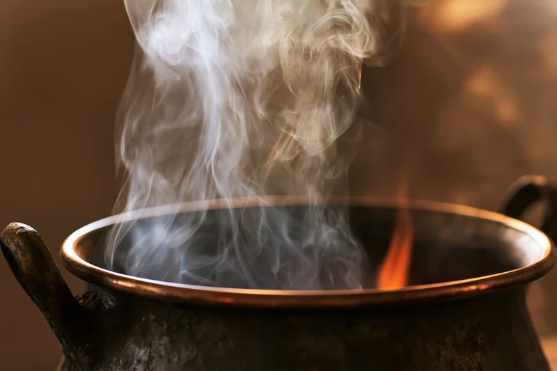 Weathered brass cauldron with steam rising over fire in dark setting