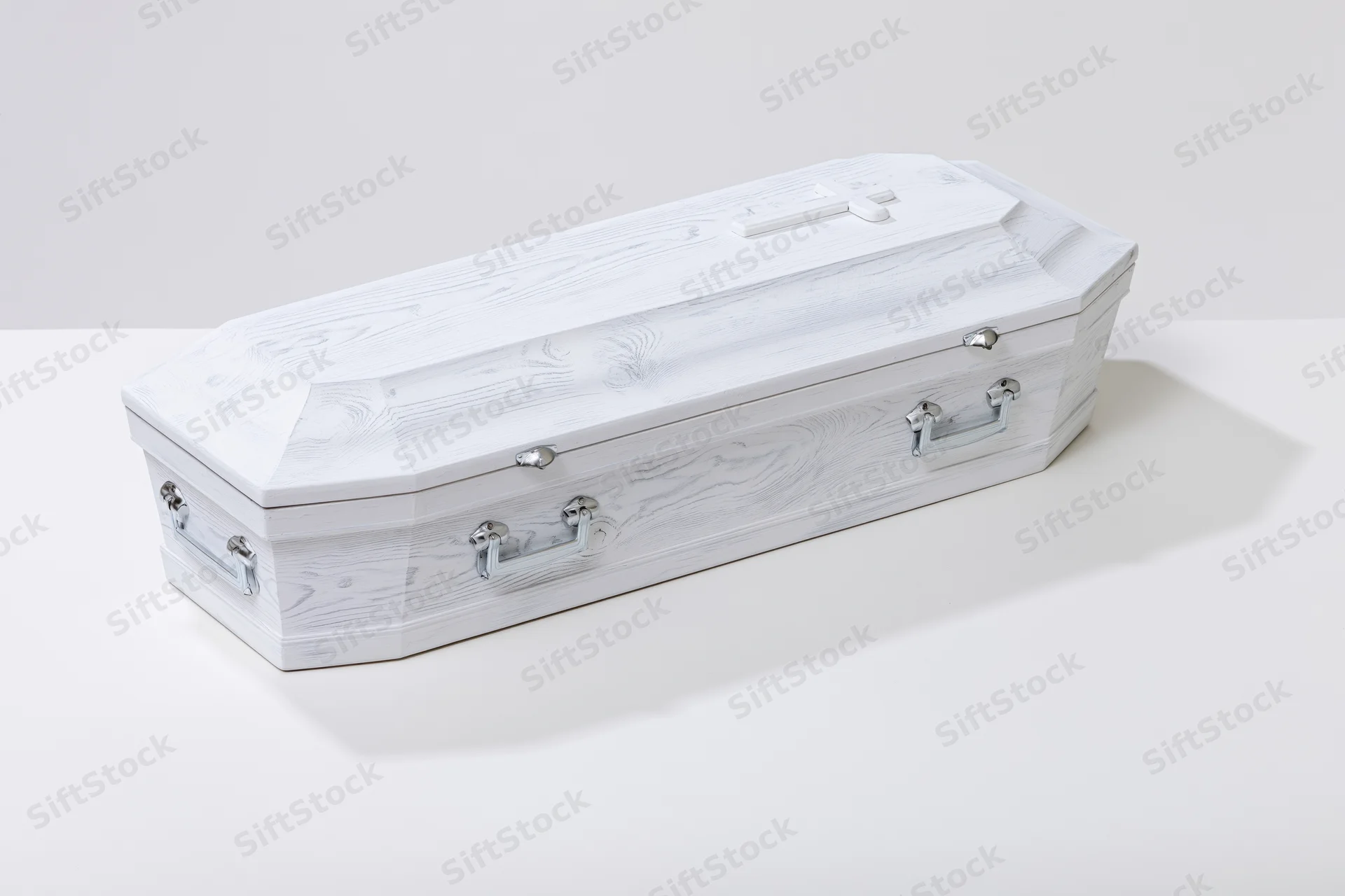 White painted wooden coffin with silver handles on a plain white surface