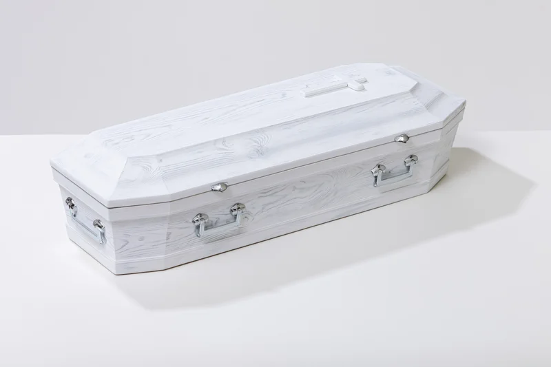 White painted wooden coffin with silver handles on a plain white surface