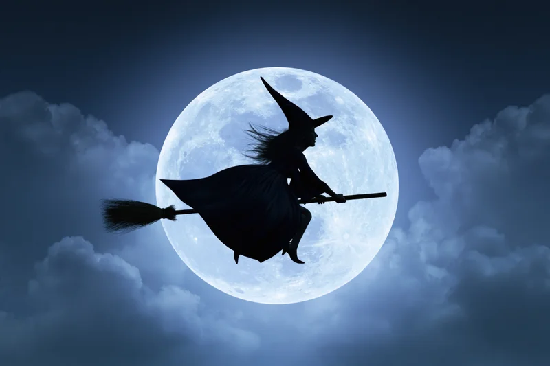 Witch silhouette flying on broomstick against full moon in cloudy night sky
