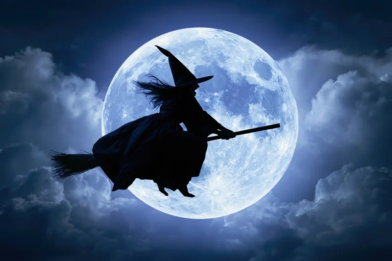 Witch silhouette flying on broomstick against full moon in cloudy night sky
