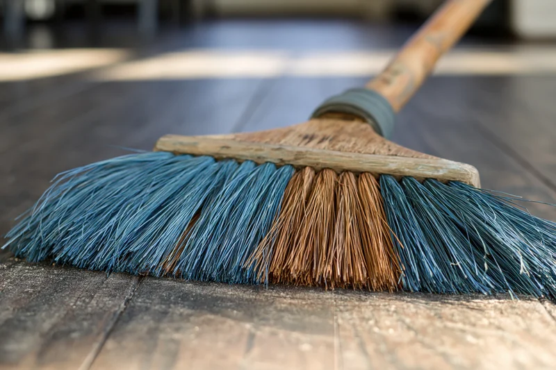 Wooden-handled broom with blue and brown bristles resting on hardwood floor
