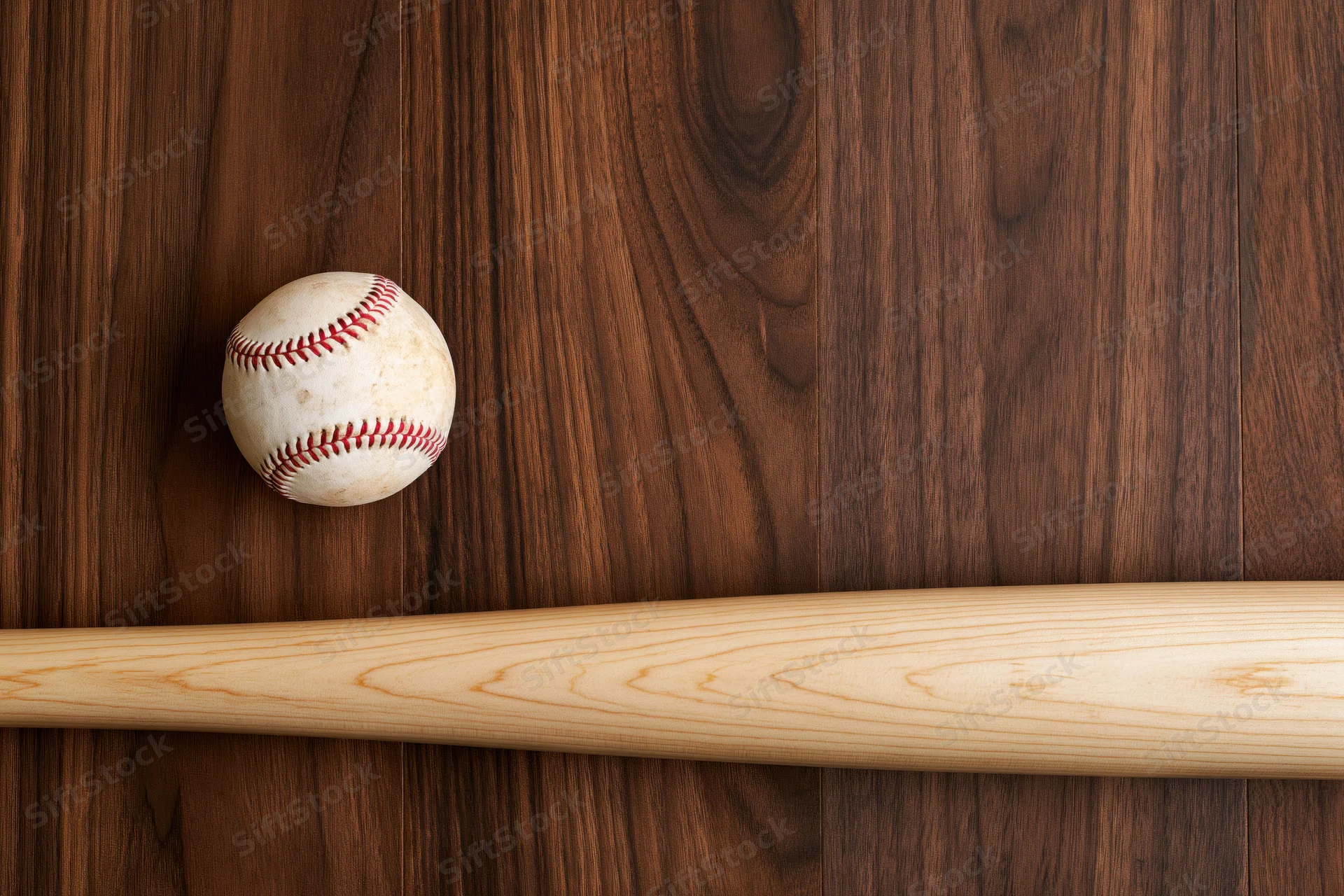 Wooden baseball bat and white leather baseball with red stitching resting on dark wood surface