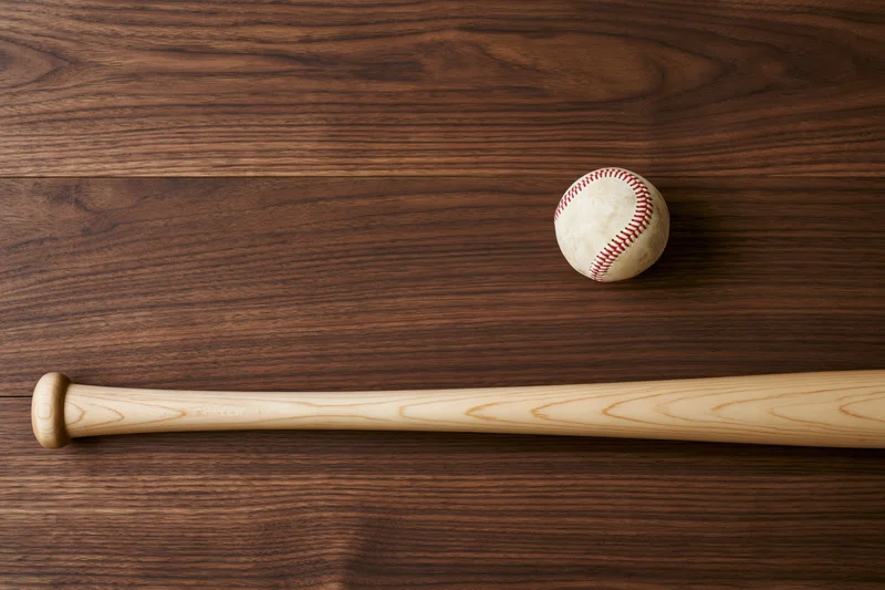 Wooden baseball bat and white leather baseball with red stitching resting on dark wood surface