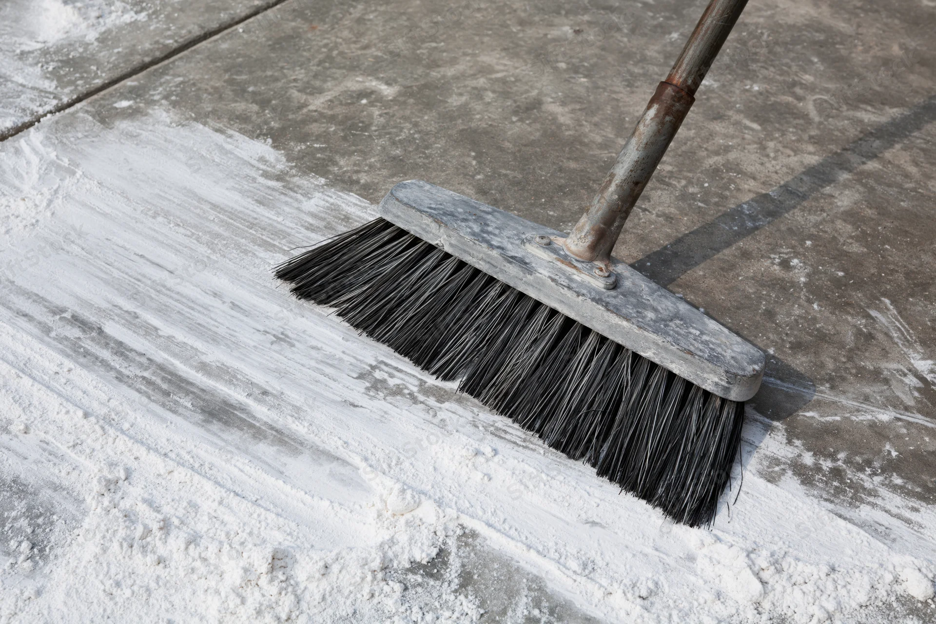 Worn push broom sweeping white powder on concrete floor