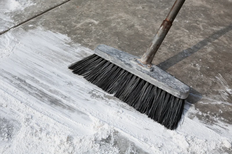 Worn push broom sweeping white powder on concrete floor