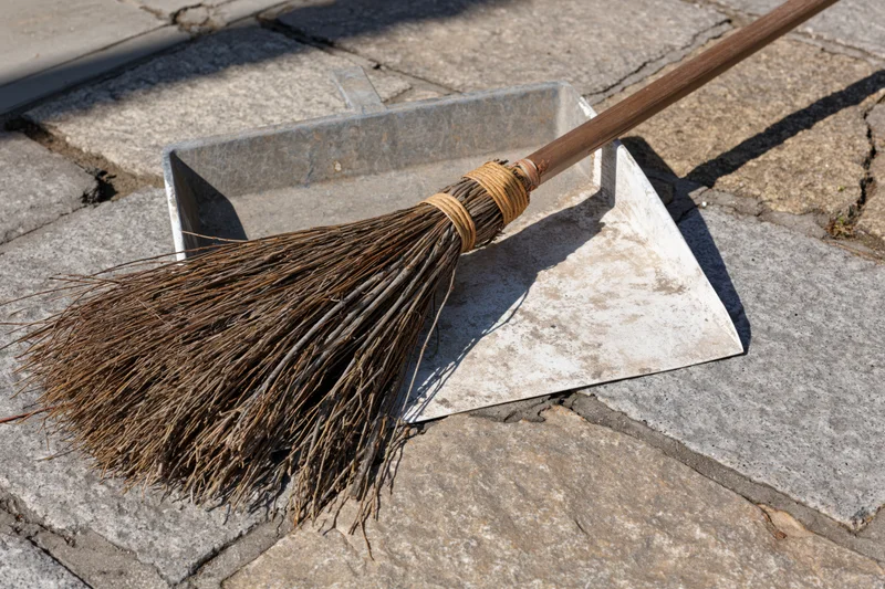 Worn twig broom resting on metal dustpan on stone pavement