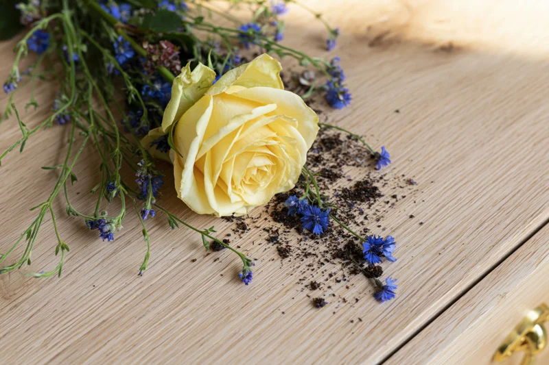 Yellow rose with blue wildflowers arranged on a wooden surface