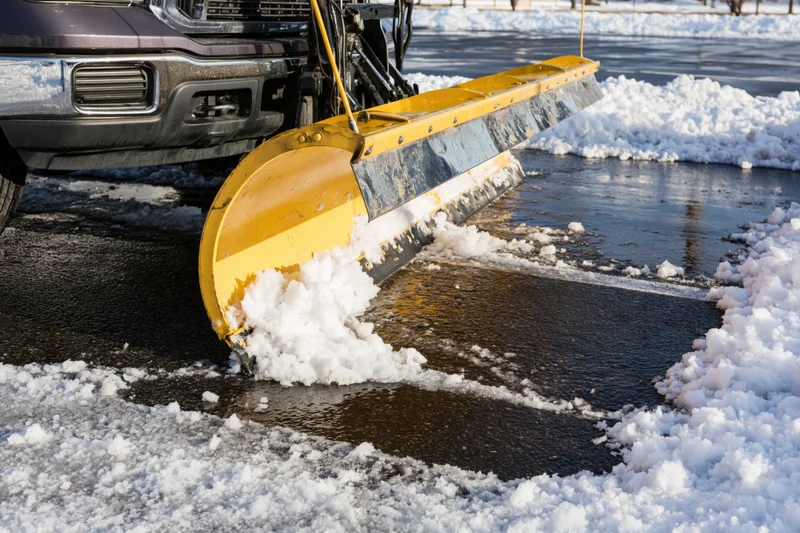 Yellow snow plow blade clearing snow from asphalt road