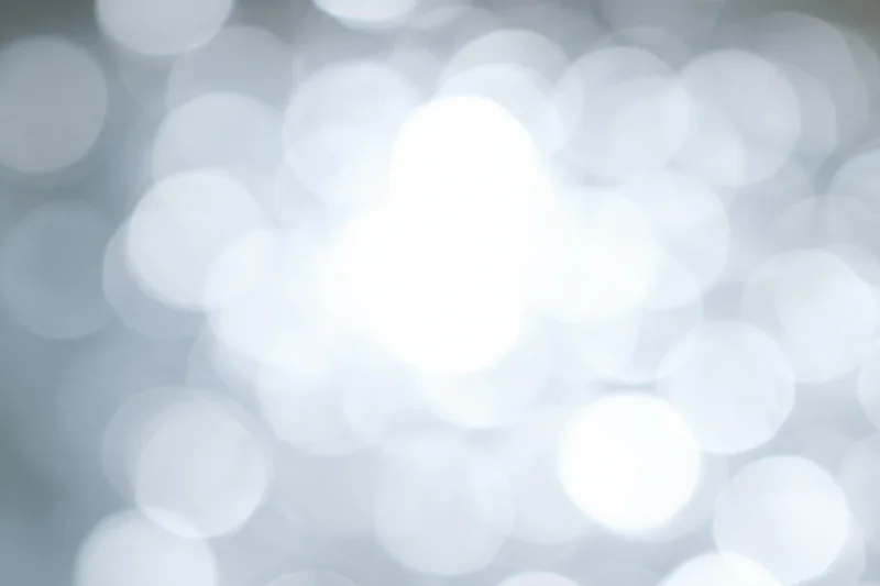 Abstract bokeh background with soft white and gray glowing circles, defocused lights creating a festive atmosphere