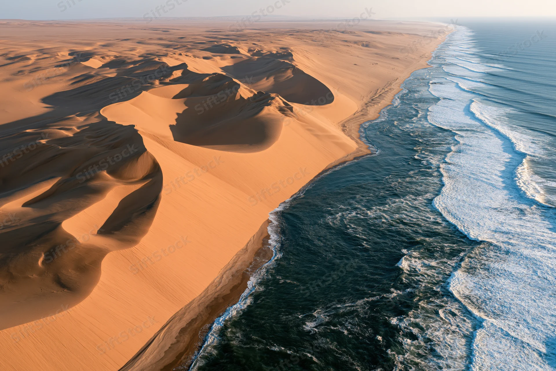 Aerial view of namib desert coastline with orange sand dunes meeting blue ocean waves