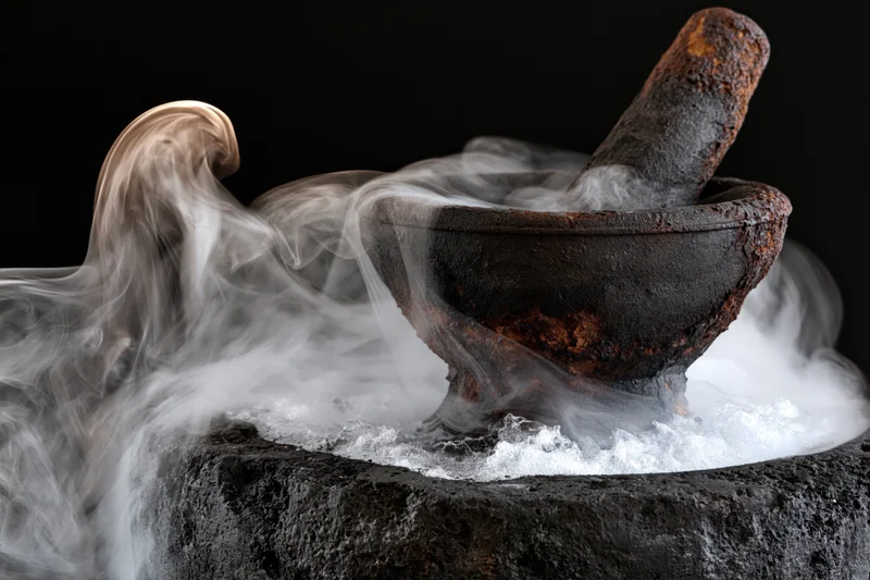 Aged rusty stone mortar and pestle emitting thick smoke on black background