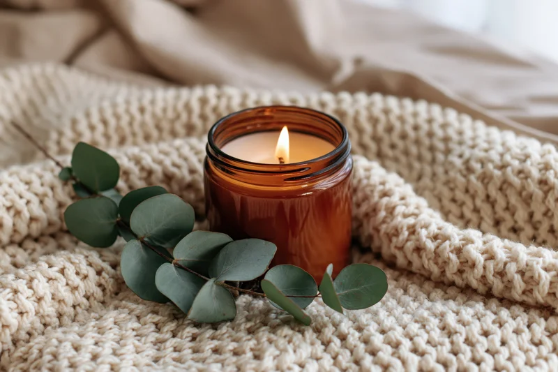 Lit amber glass candle with eucalyptus leaves on a knitted beige blanket