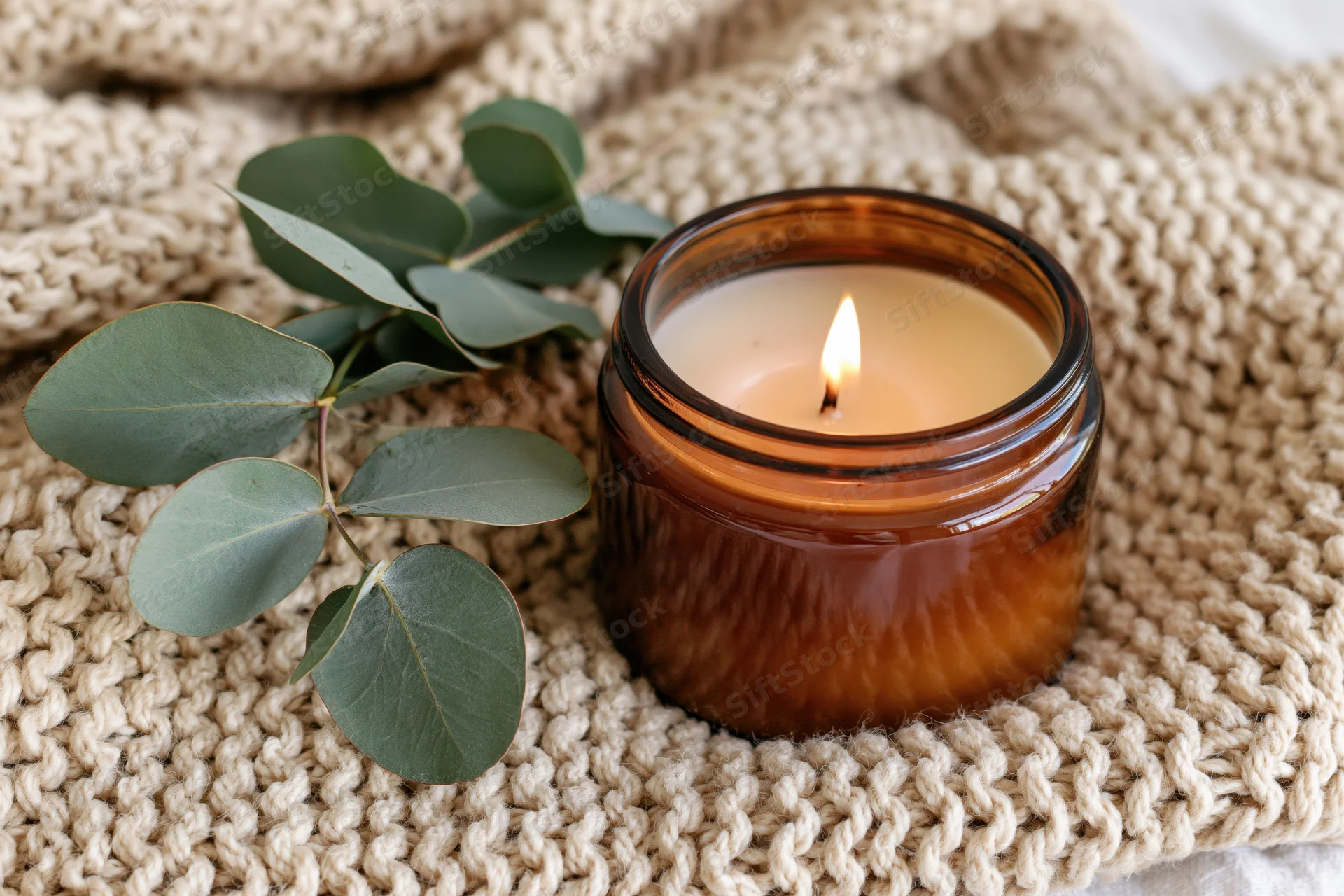 Lit amber glass candle with eucalyptus leaves on a knitted wool blanket