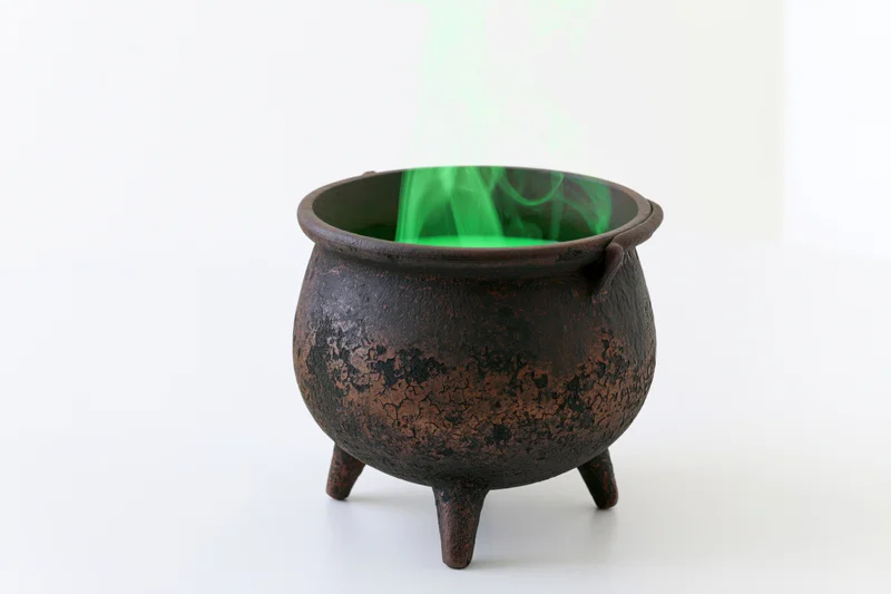 Old cast iron witch's cauldron with green smoke rising from it on white background
