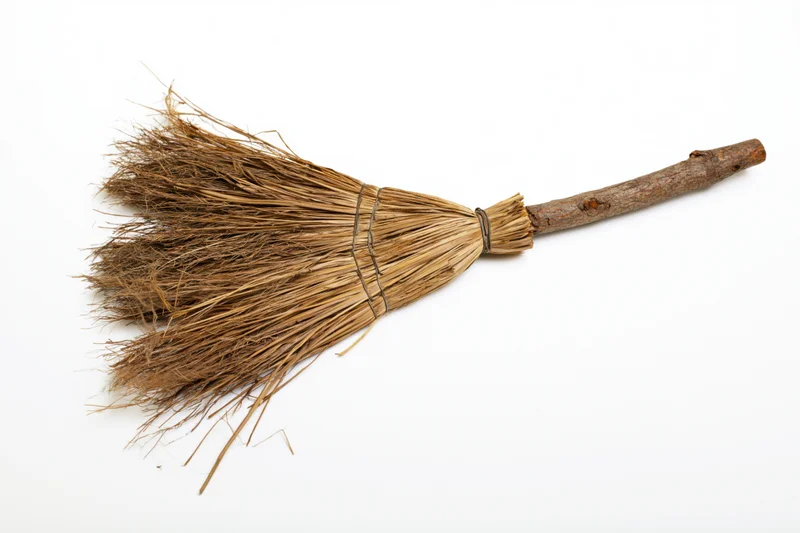 Old handmade straw broom lying diagonally on white background
