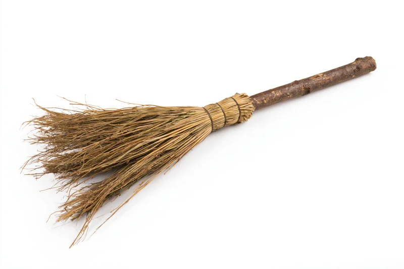 Old handmade straw broom lying diagonally on white background