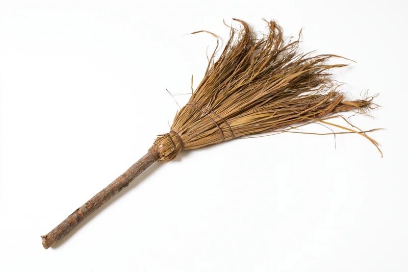 Old handmade straw broom lying diagonally on white background