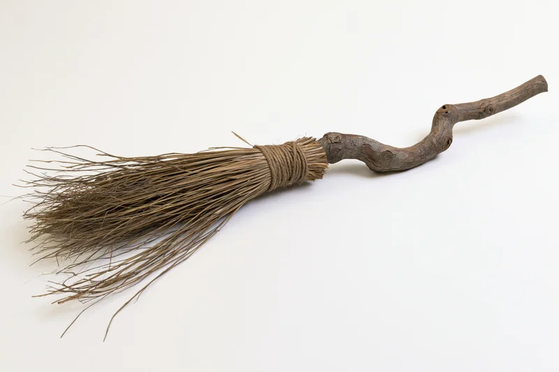 Old handmade witch's broom with wooden handle and straw bristles lying diagonally on white background