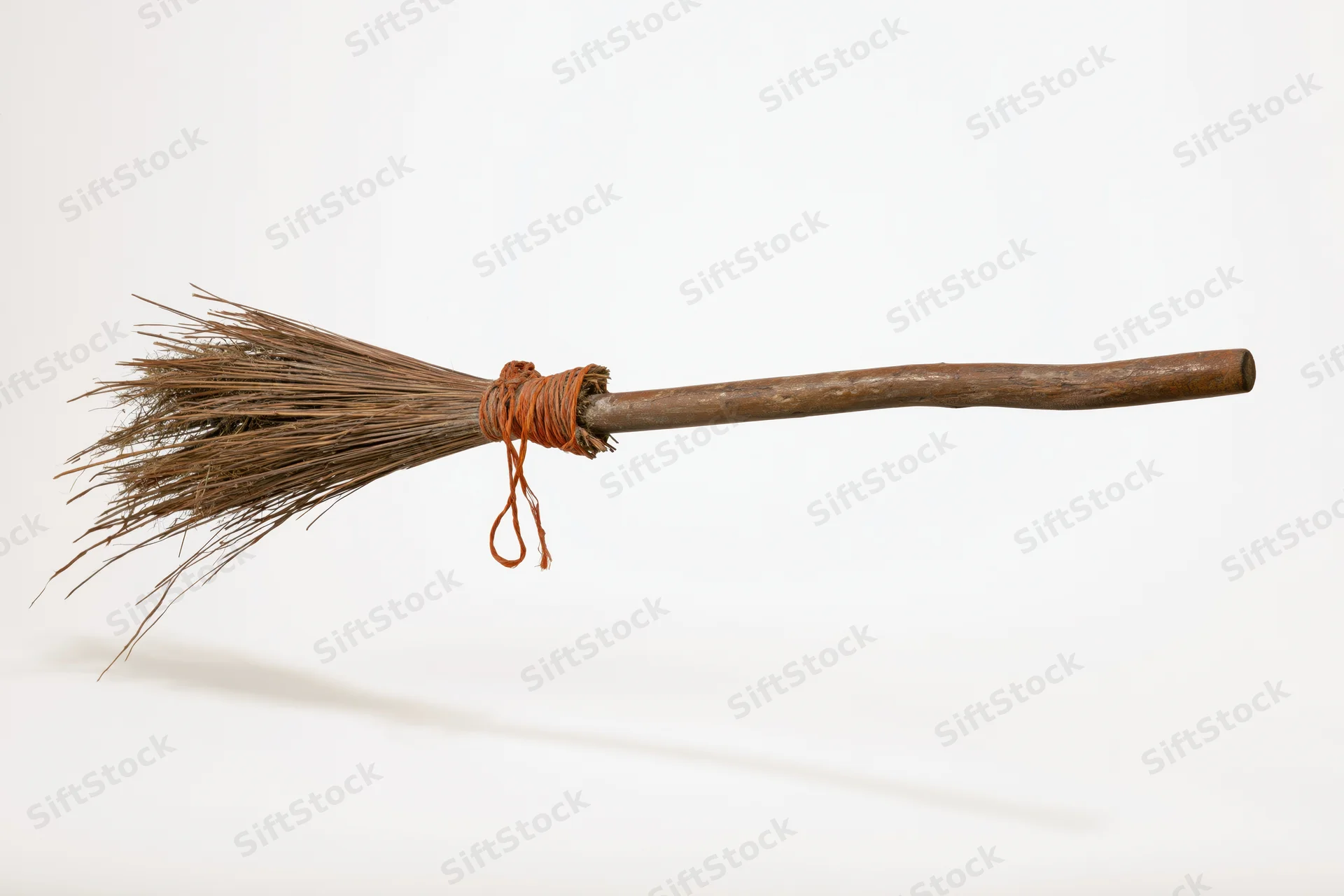 Old rustic witch's broom with dried straw bristles tied to wooden handle on white background