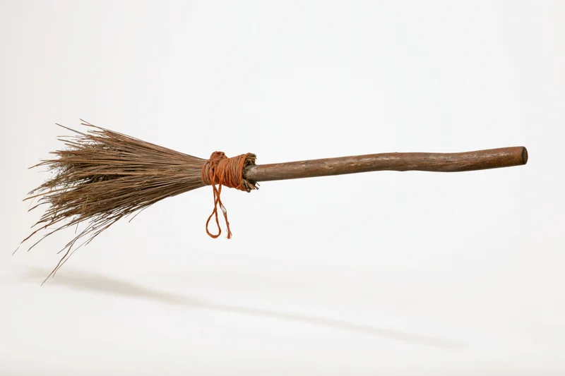 Old rustic witch's broom with dried straw bristles tied to wooden handle on white background