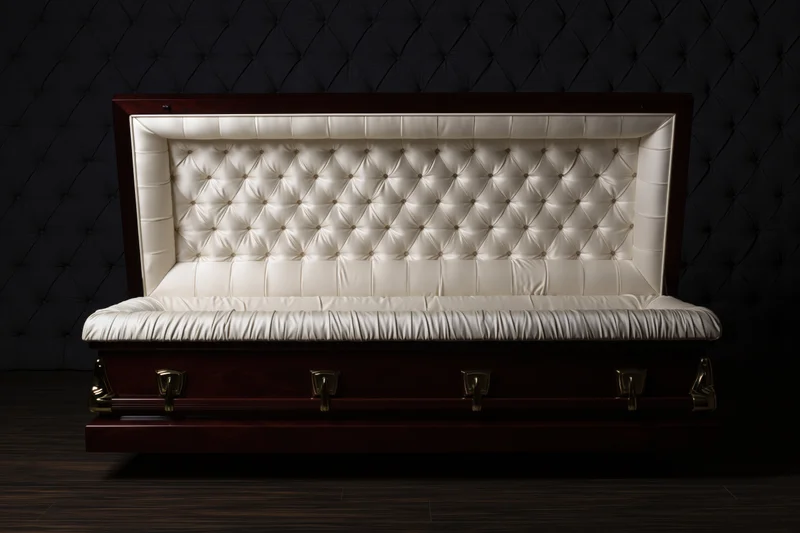 Open mahogany casket with cream tufted upholstery in dark interior