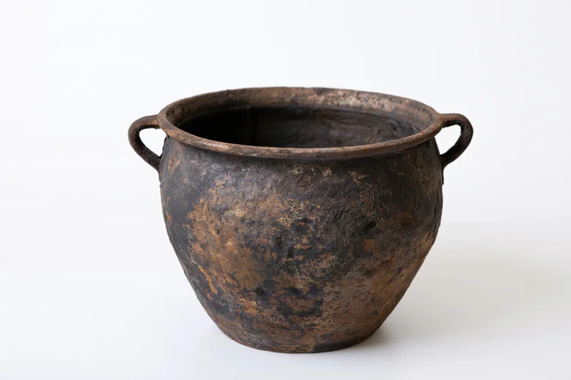 Antique black clay cooking pot with two small loop handles on white background