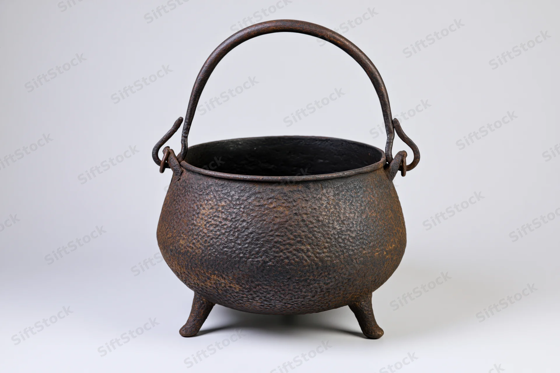 Antique cast iron cauldron with curved bail handle and three legs on white background