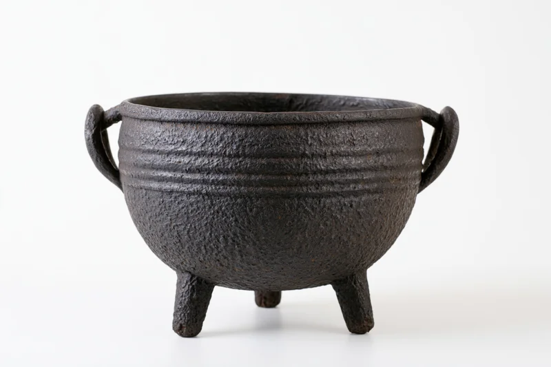 Antique cast iron cauldron with three legs and side handles on white background