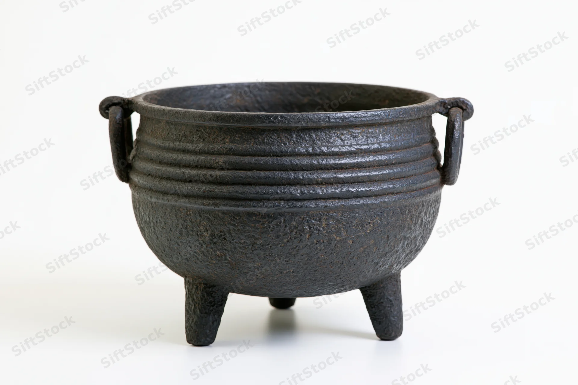 Antique cast iron cauldron with three legs and side handles on white background